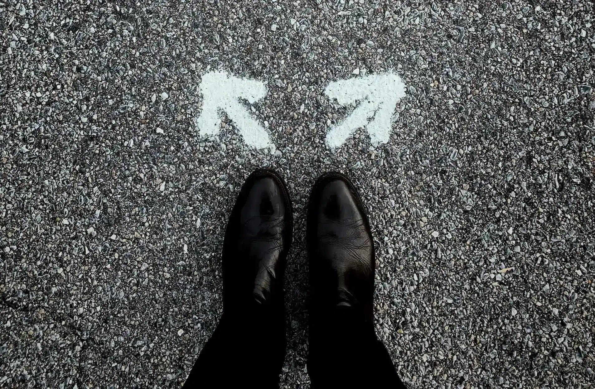 Person standing at a road fork marked by arrows pointing in opposite directions