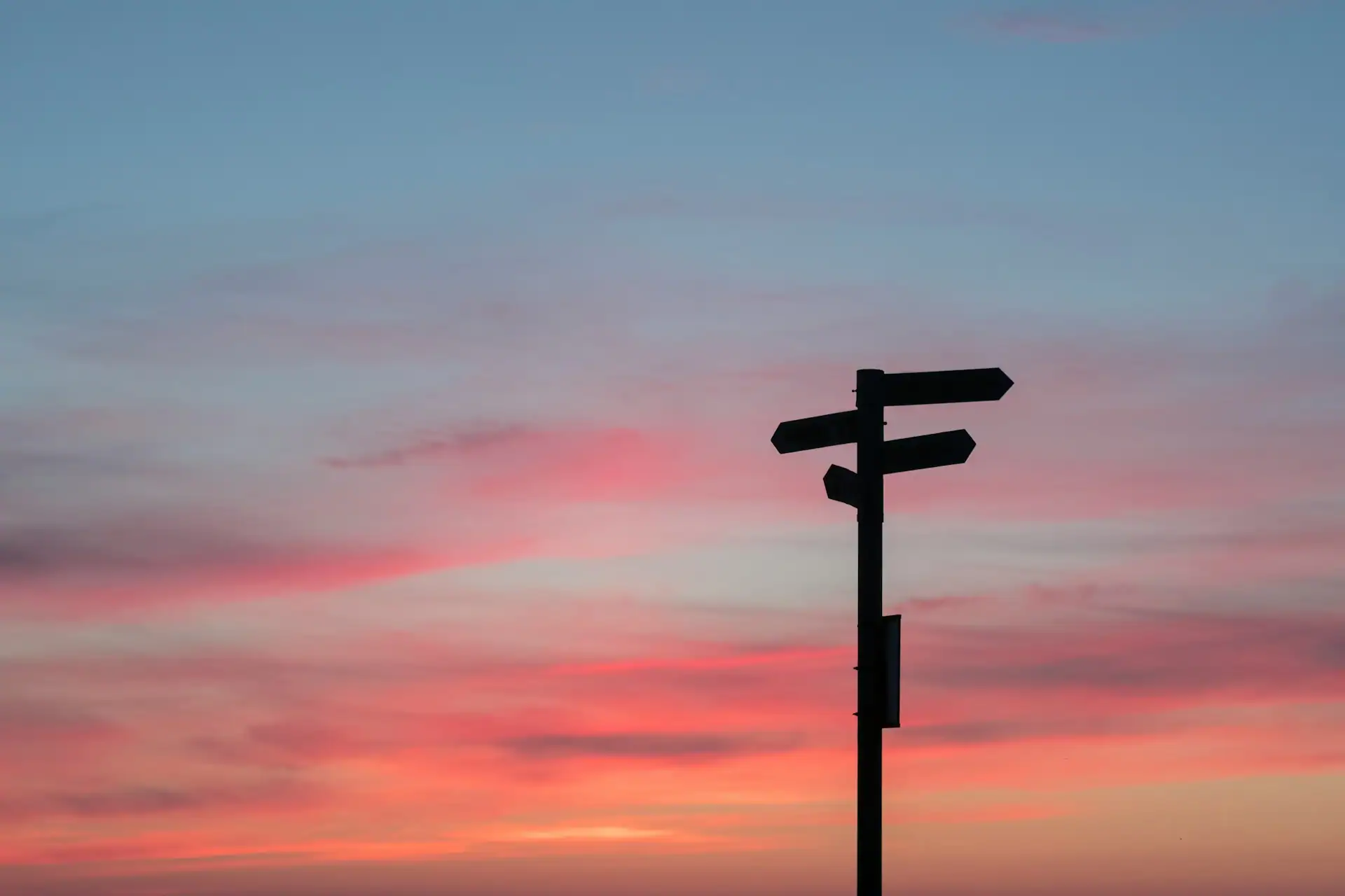 Silhouette of a multi-directional signpost against a sunset sky